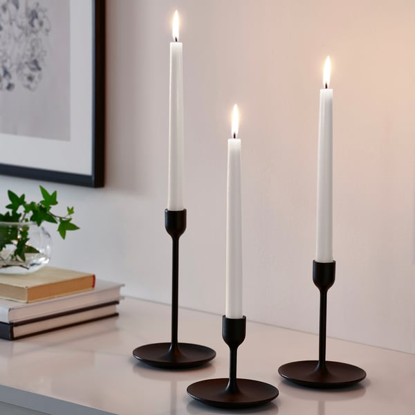 Tre KLOKHET svarta ljusstakar med vita ljus. Smal, cylindrisk design, liten storlek i förhållande till böcker och vas.