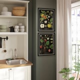 KNOPPÄNG-tavlor med fruktkonst hänger ovanför diskbänken och ger livfull färg till den mörkgröna väggen.