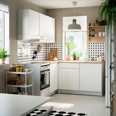 Modernt l-kök: vita skåp, träbänk, prickig backsplash, vitvaror i rostfritt stål, växter.