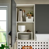 Öppet köksskåp med tallrikar, skålar och en vattenkokare på hyllor.