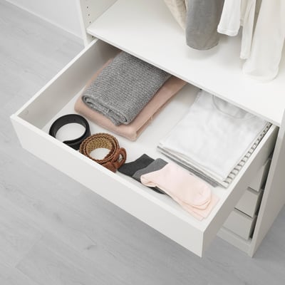 Öppen garderobslåda med prydligt vikta kläder och accessoarer. Minimalistisk, svagt upplyst förvaring.