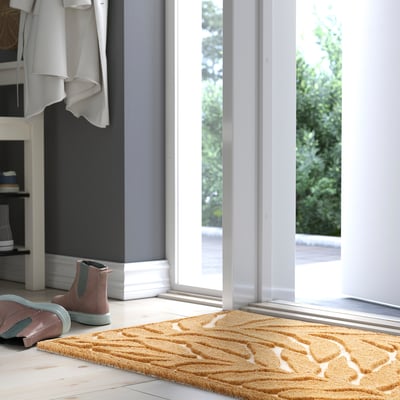En KONTANTER brun dörrmatta med vita blad, effektiv mot smuts.