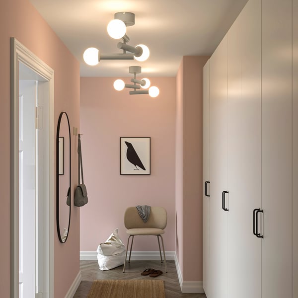 Modern hall med KRANBALK taklampa, rosa väggar, trägolv, spegel, väskkrok, stol och garderob. Bländfri belysning.