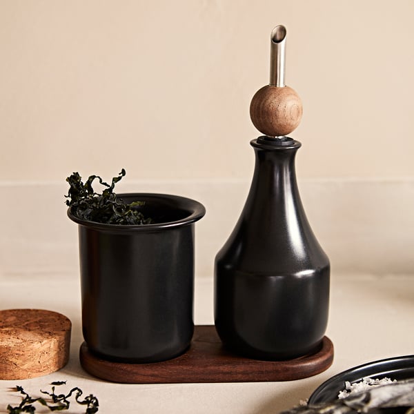 Keramisk oljedispenser och kopp med tång på träbricka