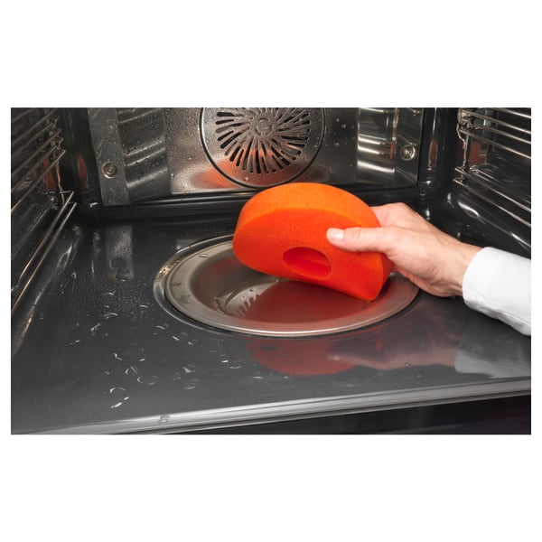 Rengöring av ugnen med orange svamp och tvålvatten, som visar dess yta i rostfritt stål som är lätt att rengöra.