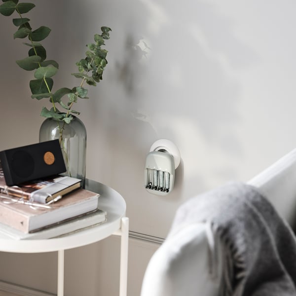 Minimalistiskt vardagsrum med ett sidobord, vas, böcker och batteripaket. Personers axlar synliga.