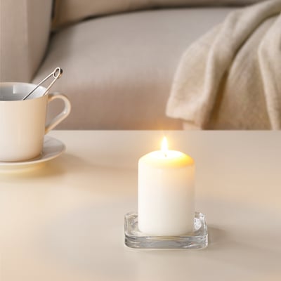 Tänd vitt ljus i genomskinlig hållare bredvid vit kaffekopp, vilket skapar mysig atmosfär.