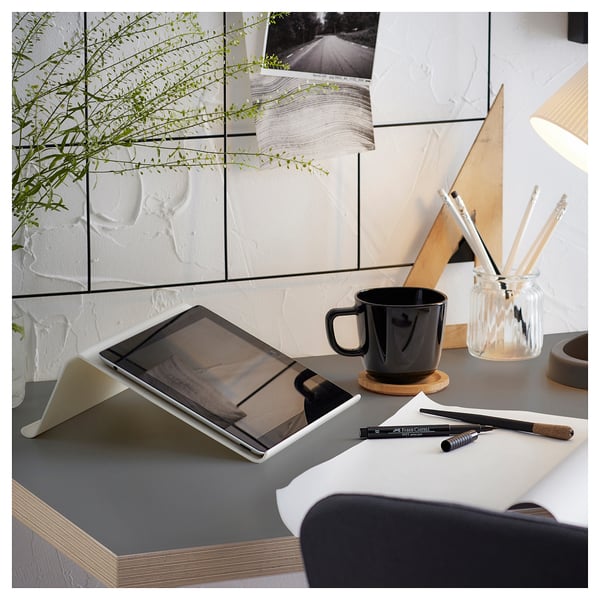 Arbetsbord med surfplatta, svart mugg, pennor och växt. Ren, modern design med vit bordsskiva och träben.