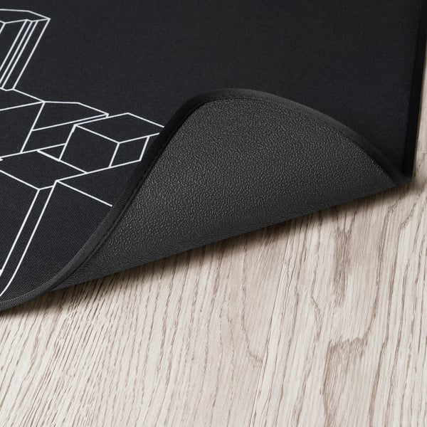 Svart golvmatta för spelstolar med vit geometrisk design, tjock slitstark gummibaksida, lagd på trägolv.