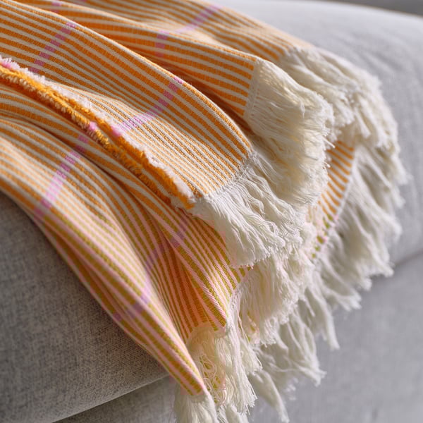 Lätt vävd bomullspläd med ljusa orange och rosa ränder, fransiga kanter, draperad över en yta.