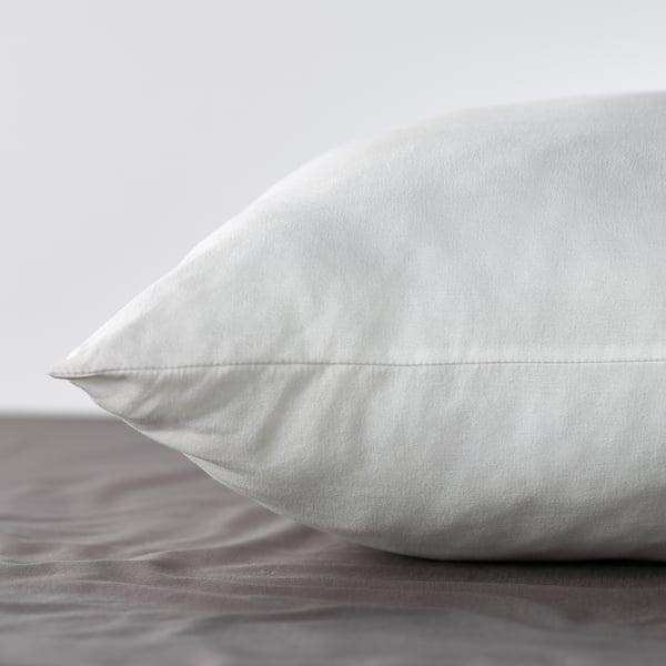 Närbild av en fluffig vit kudde med slätt, strukturerat tyg på en säng.
