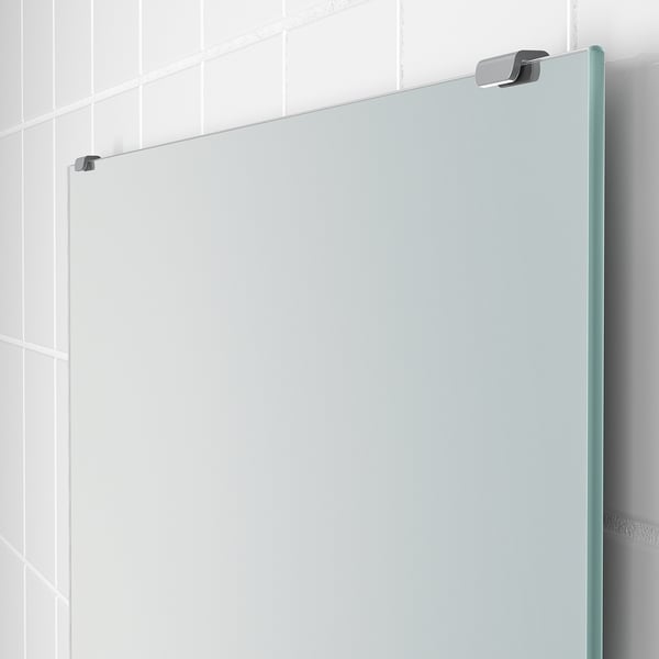 Modern kantlös spegel monterad på vit kaklad vägg med eleganta metallarmaturer.