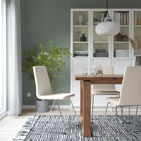 Modern matplats med beige stol LILLÅNÄS, träbord, vit taklampa, grå matta och bokhylla med blå vas.