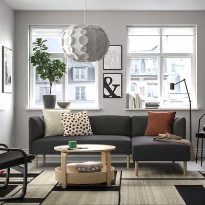 Modernt vardagsrum med grå LILLEHEM modulsoffa, mönstrade svankkuddar, soffbord i trä, stora fönster och hängande armatur.