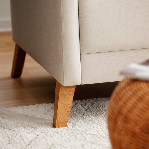 Modern beige soffa med rena linjer, rejäla träben och en mysig kudde på en texturerad matta.