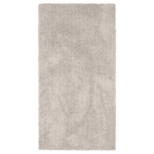 En rektangulär, beige matta LINDKNUD. Den är tillverkad av återvunnen polyester och har en mjuk, plyschyta som är idealisk för sovrum.