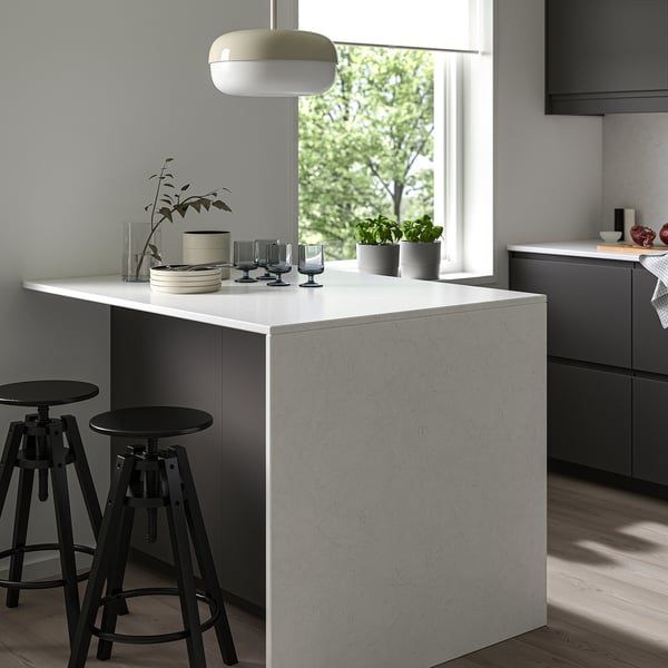 Minimalistiskt kök med bänkskiva i återvunnet glas, svarta pallar, taklampa och grå skåp.