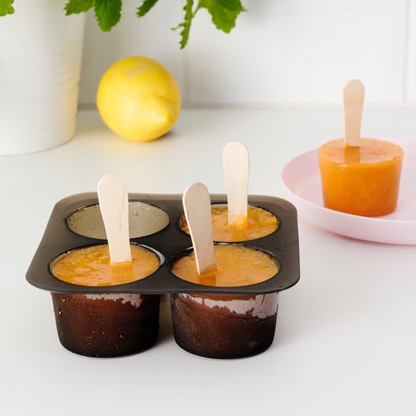 Iskubsbricka med orange vätska och pinnar, plus en fryst pop-on-hållare.