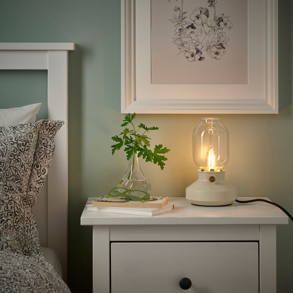 Sovrum med LUNNOM-lampa, blommigt tryck och säng med prydnadskudde och böcker.