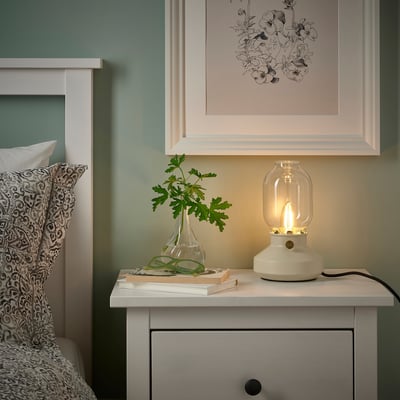 Sovrum med LUNNOM-lampa, blommigt tryck och säng med prydnadskudde och böcker.