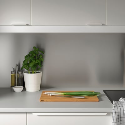 Minimalistisk grå köksbänk. Liten krukväxt, oljeflaskor, kniv, salladslök och skärbräda med väggpanel LYSEKIL.
