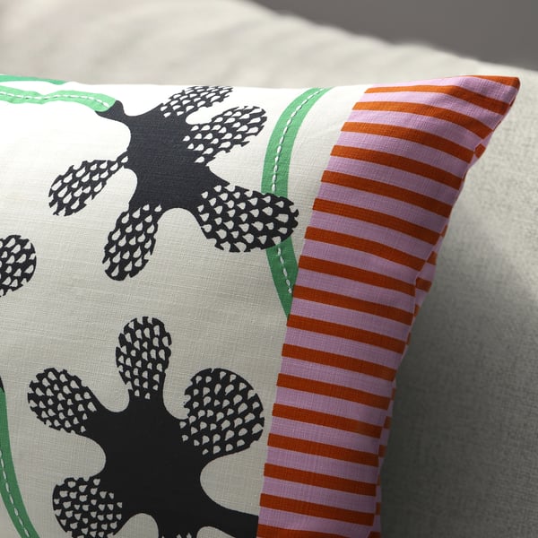 En kudde med stora svarta blommönster och ljusa vertikala ränder i rosa och orange på ena sidan, som vilar på en ljus yta.