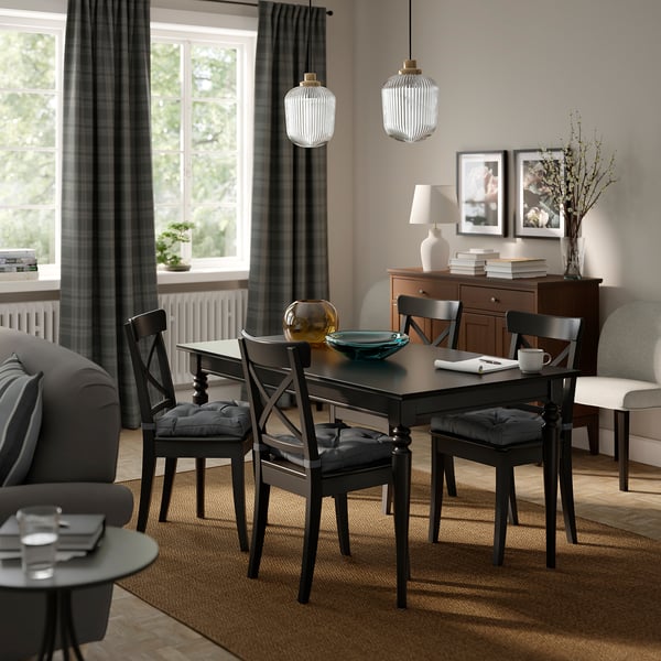 Modern matplats med svarta MALINDA-stolar , tjocka grå dynor. Träbord, pendellampor, skänk i trä och fönster med grå gardiner.