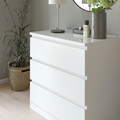 Vit MALM-kista med glasskiva, lampa, klocka, växt och vas.