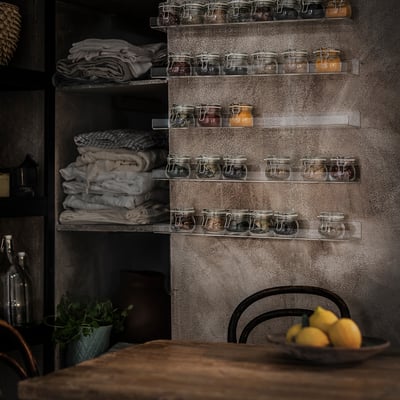 Klara flytande hyllor i akryl rymmer glasburkar med konserverade livsmedel, metallvägg, träbord med citroner och stol.