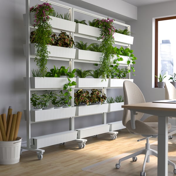 Kontor med MITTZON vit planteringsvägg, olika växter, skrivbord, stol, trägolv, utsikt över staden.