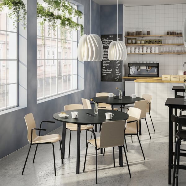 Modernt kafé med runda bord, ljusa stolar, stora fönster och hängande lampor.