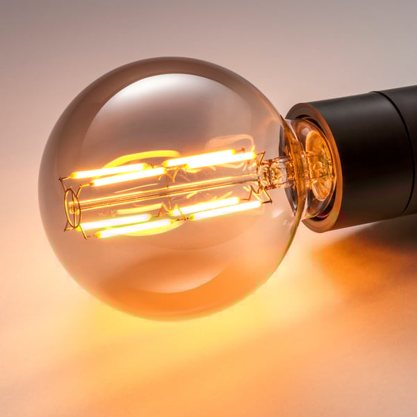 Globe LED-lampa med åtta glödande glödtrådar i rökfärgat glas som avger varmt ljus.