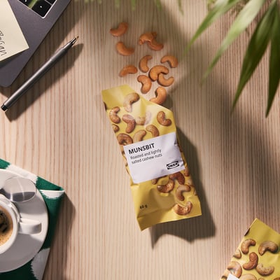 Påse med IKEA MUNSBIT cashewnötter på skrivbordet med kaffe och anteckningsbok