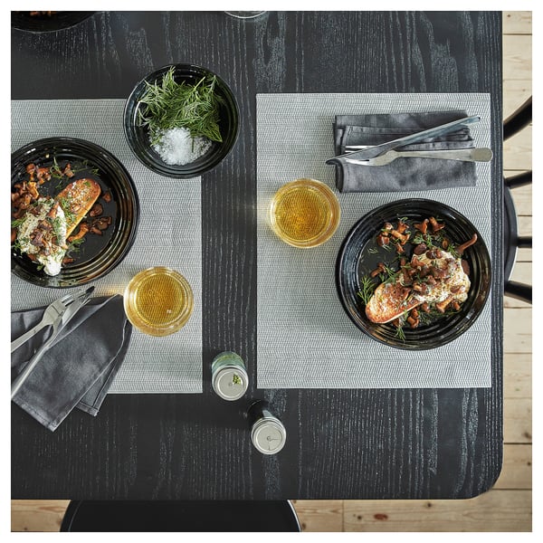 Middagsuppställning med två tallrikar med fisk, lök och örter; två glas, bestick och en kryddfat på ett mörkt träbord.