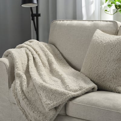 Beige NÄTNÄVA filt och kudde på grå soffa som skapar en mysig atmosfär.