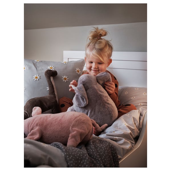 Ung flicka kramar grå plysch elefantleksak på sängen med vita prästkragar. Mysigt och varmt.