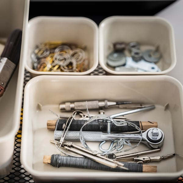 Organiserad låda med NOJIG vita plastlådor som innehåller olika metallverktyg och klockdelar, snyggt ordnade, lämpliga för hårdvara eller urmakeri.