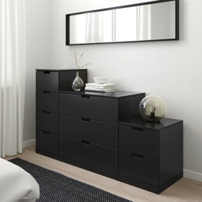 Modern NORDLI byrå med 4 lådor i det minimalistiska sovrummet. Spegel ovanför, droppformad vas på toppen, sfäriskt ljus på sidan. Elegant och organiserad.