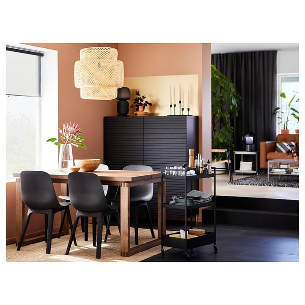 Modern matplats med svarta ODGER-stolar, träbord, hängande lampa och växter.