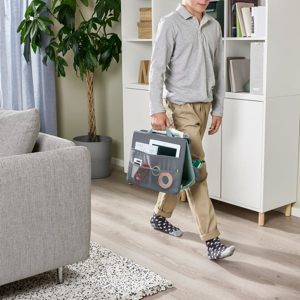 Man med grå organisatör för brevpapper och elektronik i ett ljust rum.