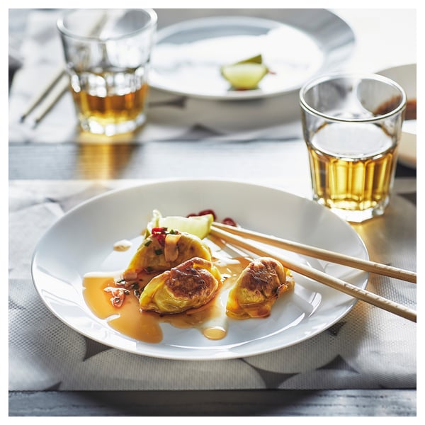 Vit glasskål med dumplings, sås och ätpinnar bredvid två glas drink.