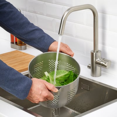 Person som tvättar sallad i diskbänk med durkslag under modern kran.
