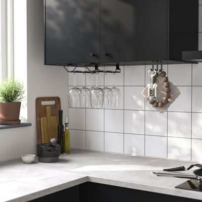 Köksbänk med vit vinglasställ PÅLYCKE som rymmer fyra glas, bredvid en växt, skärbrädor och köksredskap.