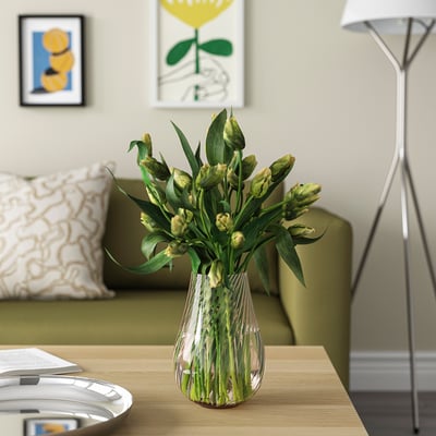 Vas av PÅSKÖTRÄD i glas med virvlar som håller gulgröna blommor på ett träbord bredvid lampa och soffa.