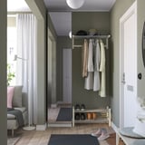 Modern entré med skohylla, klädhängare, spegel, soffa, lampa och stort fönster.