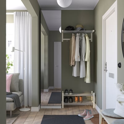 Modern entré med skohylla, klädhängare, spegel, soffa, lampa och stort fönster.