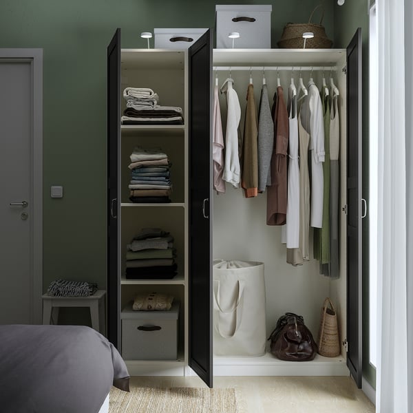 Öppen garderob med hyllor med vikta kläder och hängande plagg, med invändig förvaring och belysning.