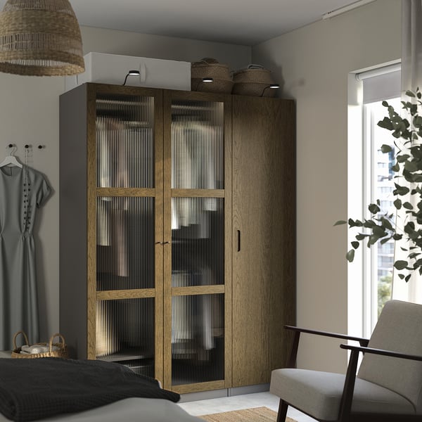 Minimalistiskt sovrum med PAX-garderob i ljust trä, nätdörrar, taklampa, fåtölj, fönster, växt.