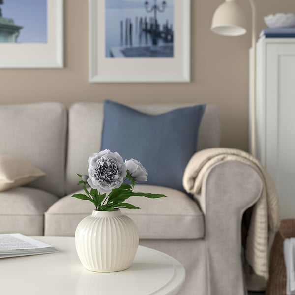 Modernt vardagsrum med beige soffa, blå kuddar, PELARBJÖRK vas med blommor och inramad väggkonst.