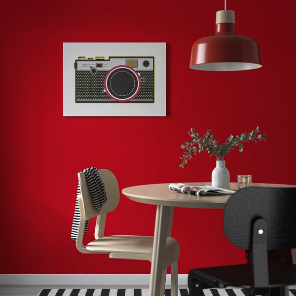 Modern matsal med djärv röd vägg, retro kamerakonst, runt bord och röd taklampa.